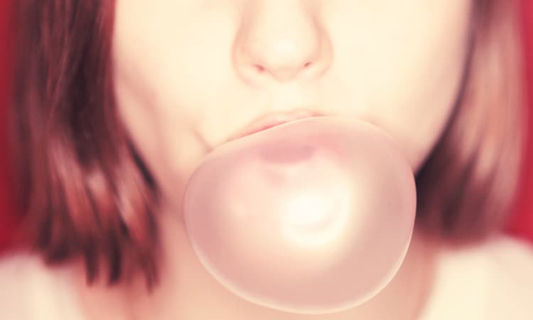 Closeup of the mouth of a red-haired woman blowing a pink sugar-free gum bubble with xylitol
