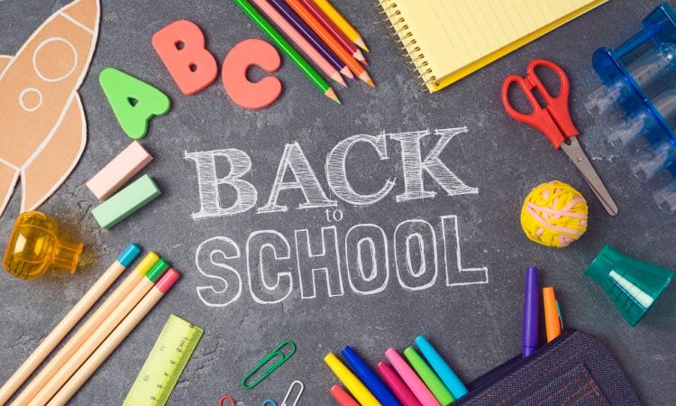 Aerial view of a black chalkboard with Back to School written in white chalk surrounded by school supplies