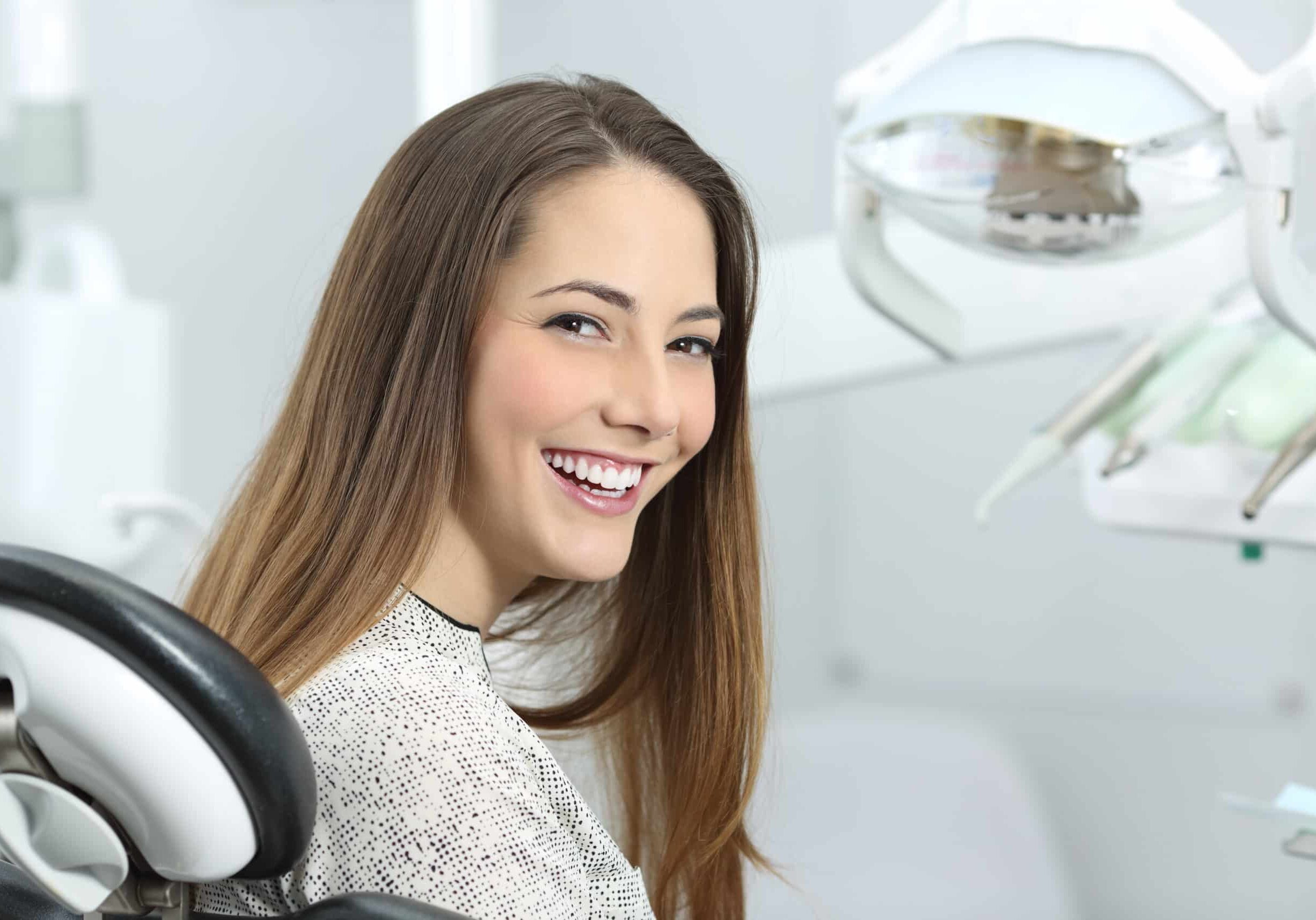 Satisfied dentist patient showing her perfect smile after treatment in a clinic box with medical equipment in the background