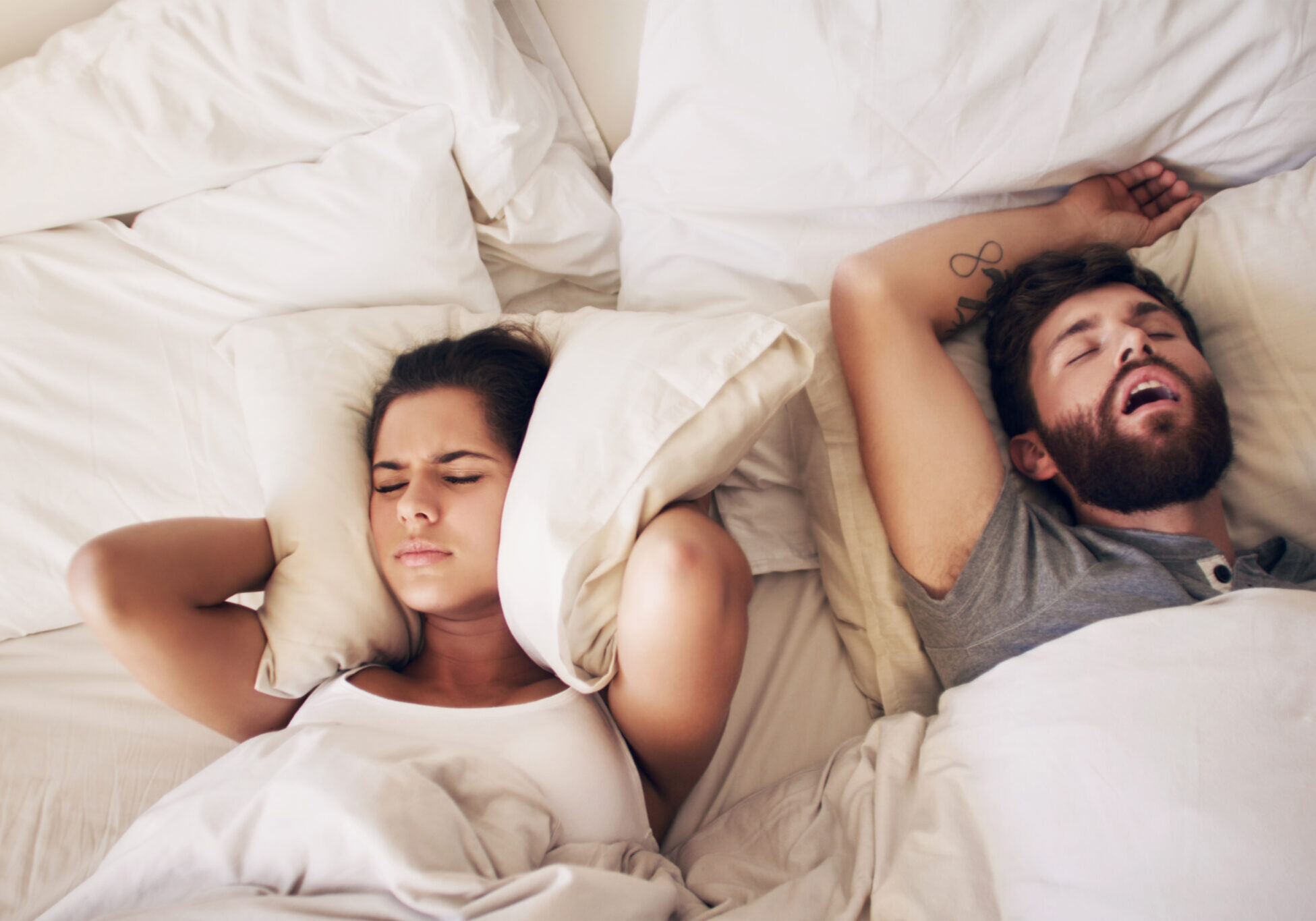 Guess who didn't get any sleep last night Shot of a young woman covering her ears with a pillow while her husband snores in bed